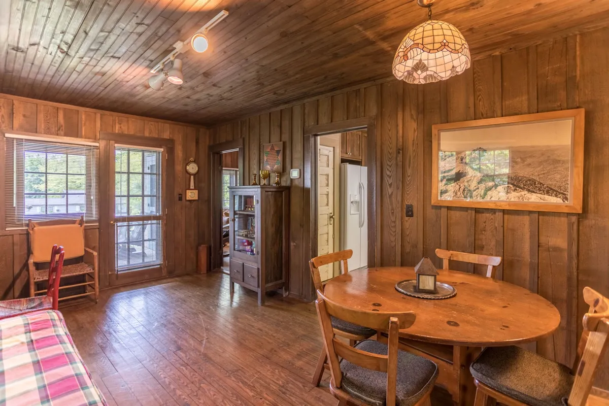 A spacious, inviting dayroom with a wooden dining table, a vintage light fixture, wooden walls, and a large window. The table is suited for family meals, board games, and social activities, while the lighting and decor add character and charm.