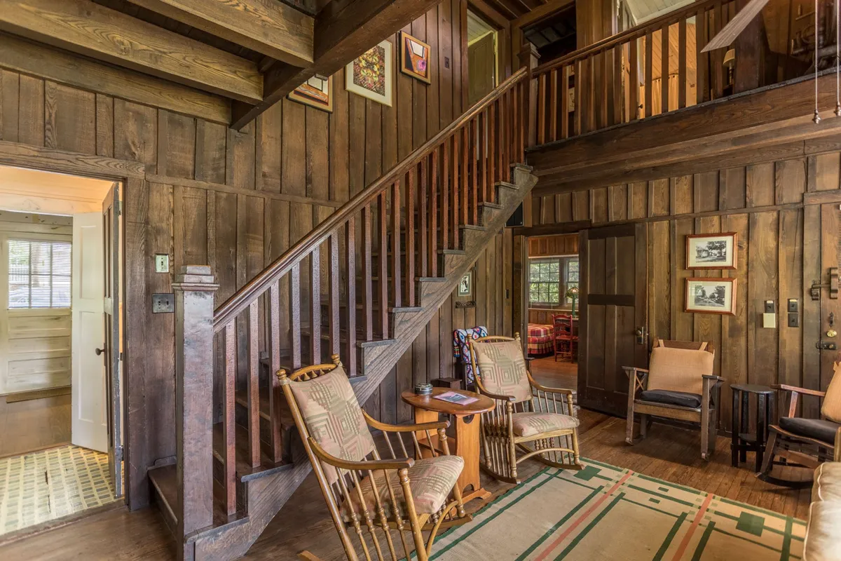 A cozy nook with classic wooden features, rocking chairs, and a staircase, offering an inviting spot for reading, socializing, or simply relaxing together. The decor exudes charm, with artwork on the walls and soft lighting.