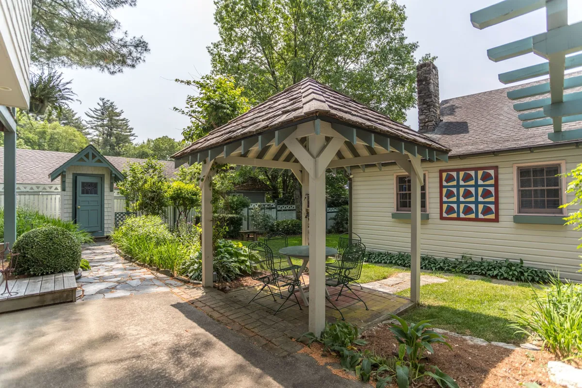 This exterior scene focuses on a charming gazebo amid a lush garden, with garden seating, colorful quilted wall art, and abundant greenery. The space suggests multiple uses: relaxing, dining, gardening, and family play. The atmosphere is relaxed and welcoming, inviting viewers to imagine outdoor gatherings and leisurely afternoons.