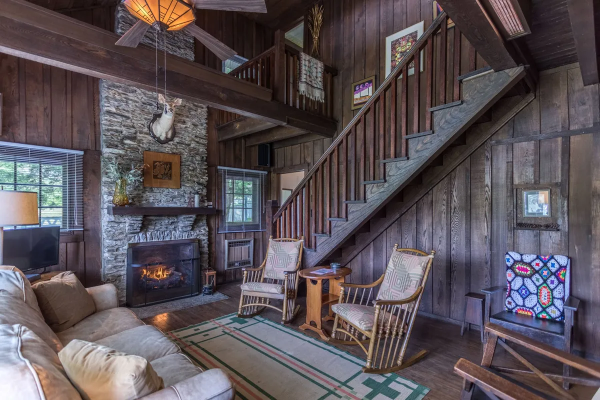 A warm, welcoming living area anchored by a central gas-log fireplace, with a cozy seating arrangement, original staircase, and tasteful wall art. The space invites relaxation, conversation, and gathering after a day of exploring nearby attractions.