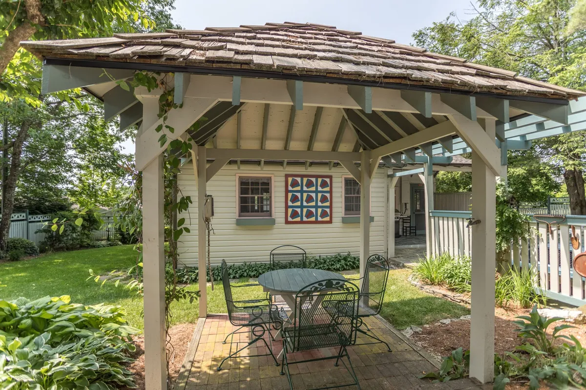 This image highlights a tranquil outdoor gathering space featuring a gazebo, vibrant wall art, and a table and chairs set amidst lush greenery. The setting suggests a spot for outdoor relaxation, al fresco dining, or social gatherings, all while appreciating local art—themes that resonate with the area's cultural richness.